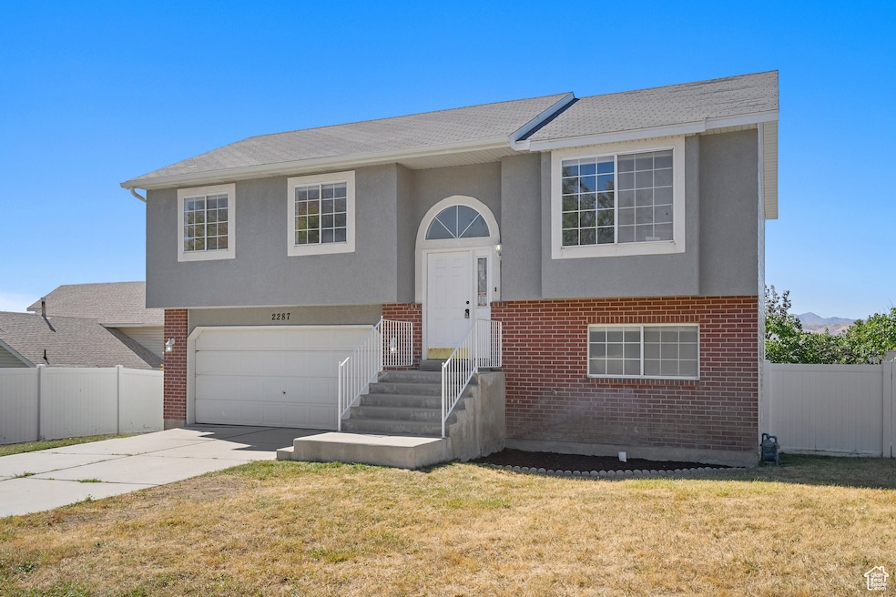 Split foyer home featuring brick siding, a garage, concrete driveway, and stucco siding