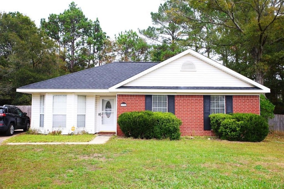 Single story home with brick siding, a shingled roof, and view of wooded area