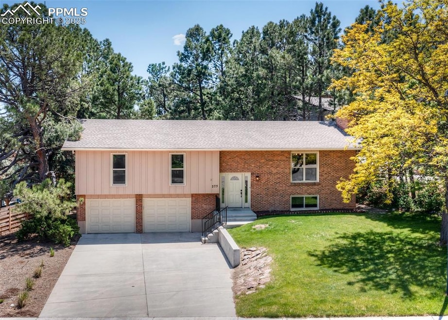 Bi-level home with a garage, driveway, brick siding, a front yard, and a shingled roof