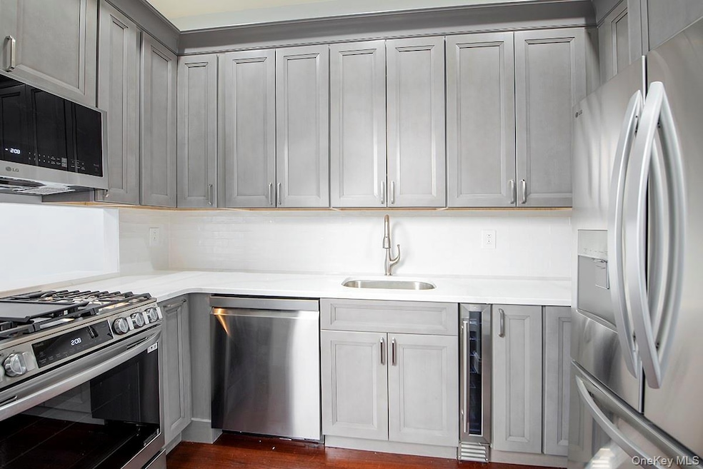 Kitchen featuring stainless steel appliances, light stone counters, beverage cooler, dark wood-style flooring, and gray cabinets