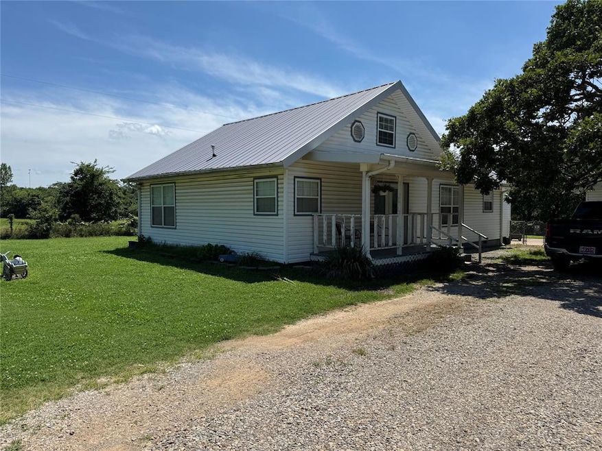 View of front of property featuring a porch, a front yard, a metal roof, and driveway