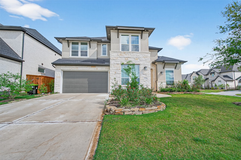 This is a modern two-story home with a stone facade and a two-car garage. It features a well-maintained lawn and landscaped garden in the front, situated in a suburban neighborhood.