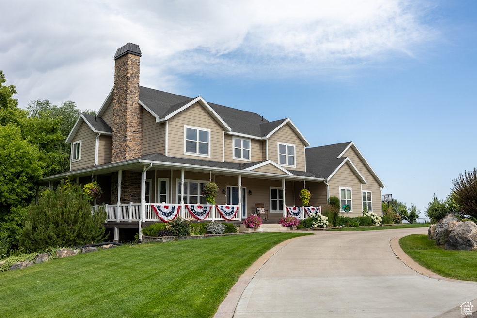 View of front of property with a front yard, covered porch, a chimney, concrete driveway, and a shingled roof