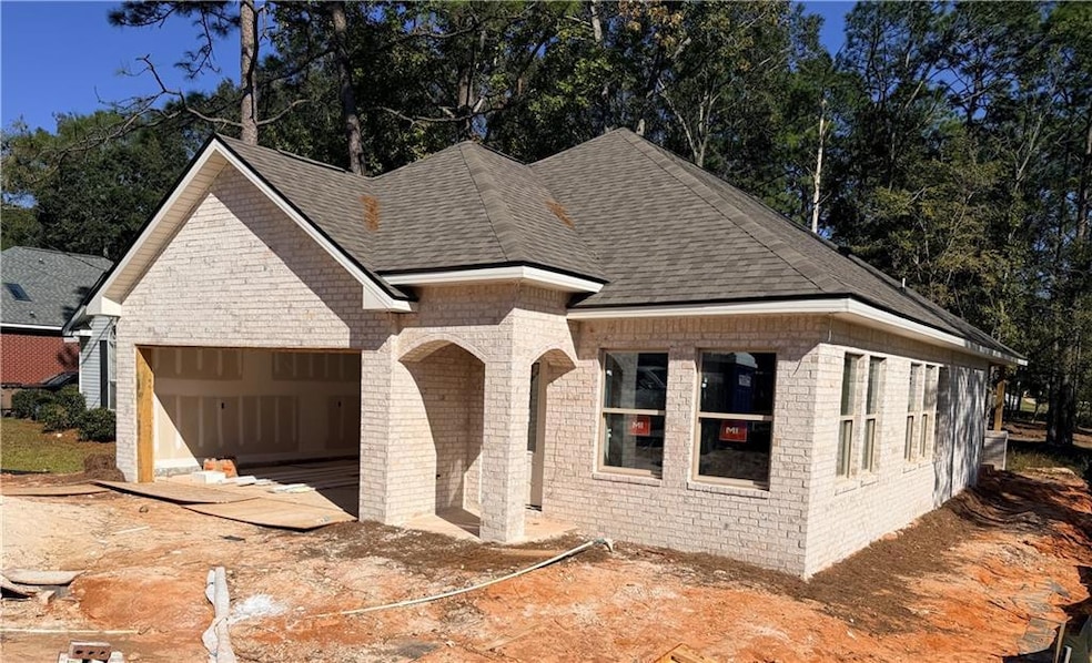 View of front of home with brick siding, a shingled roof, an attached garage, and view of scattered trees