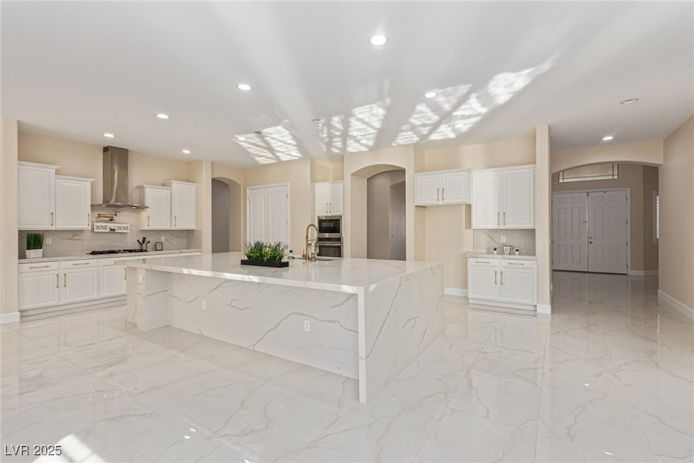 Kitchen with decorative backsplash, arched walkways, light marble finish flooring, white cabinets, and recessed lighting