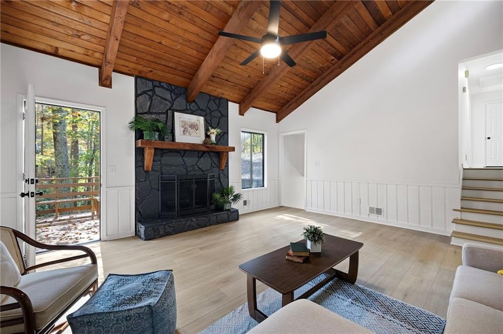 Living room featuring light wood-type flooring, wainscoting, a fireplace, a wooden ceiling with exposed beams, and a decorative wall