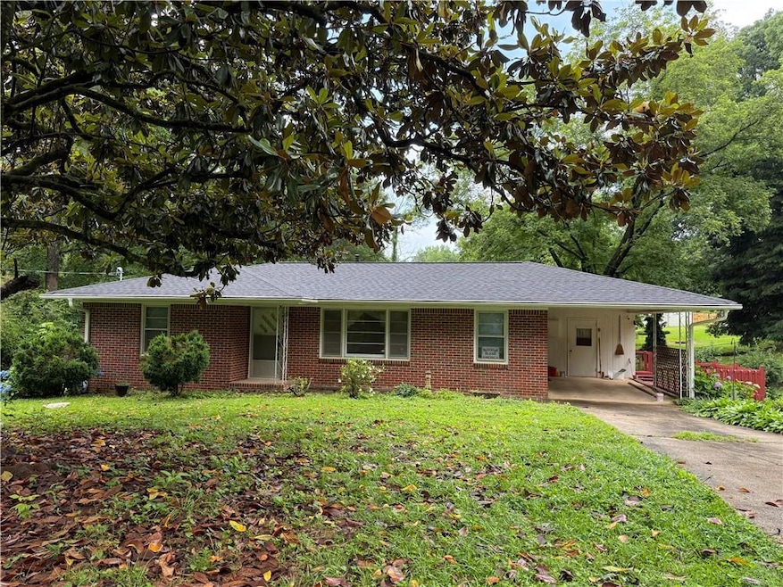Ranch-style home featuring a front lawn, an attached carport, concrete driveway, brick siding, and a shingled roof