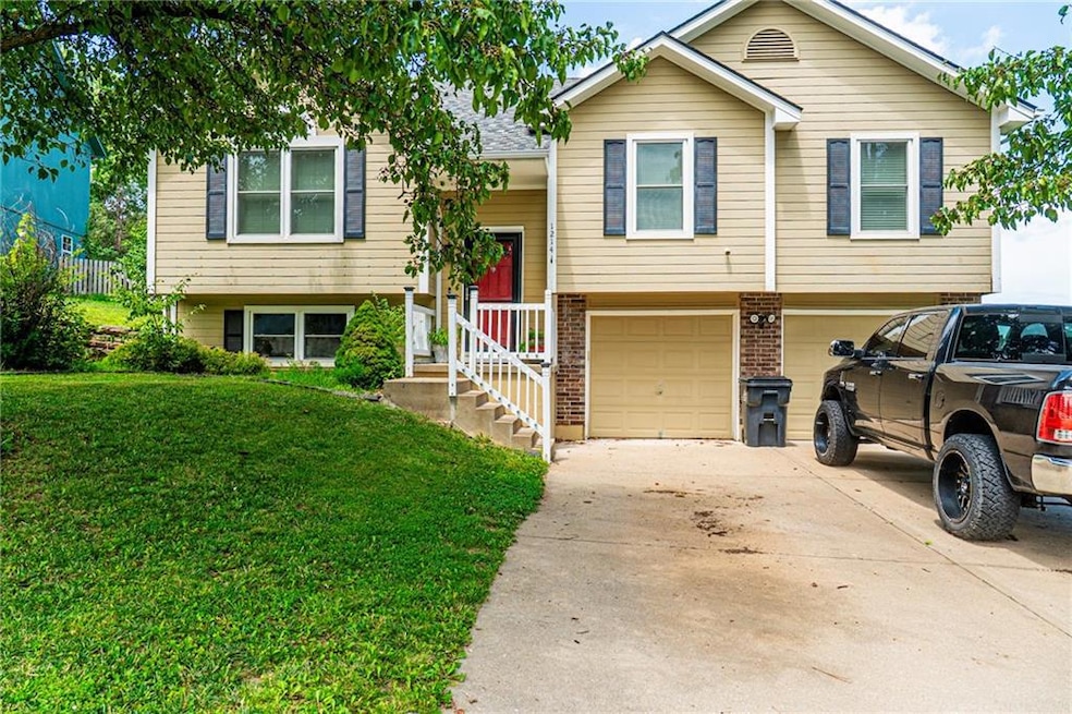 Raised ranch featuring driveway, a front yard, an attached garage, and brick siding