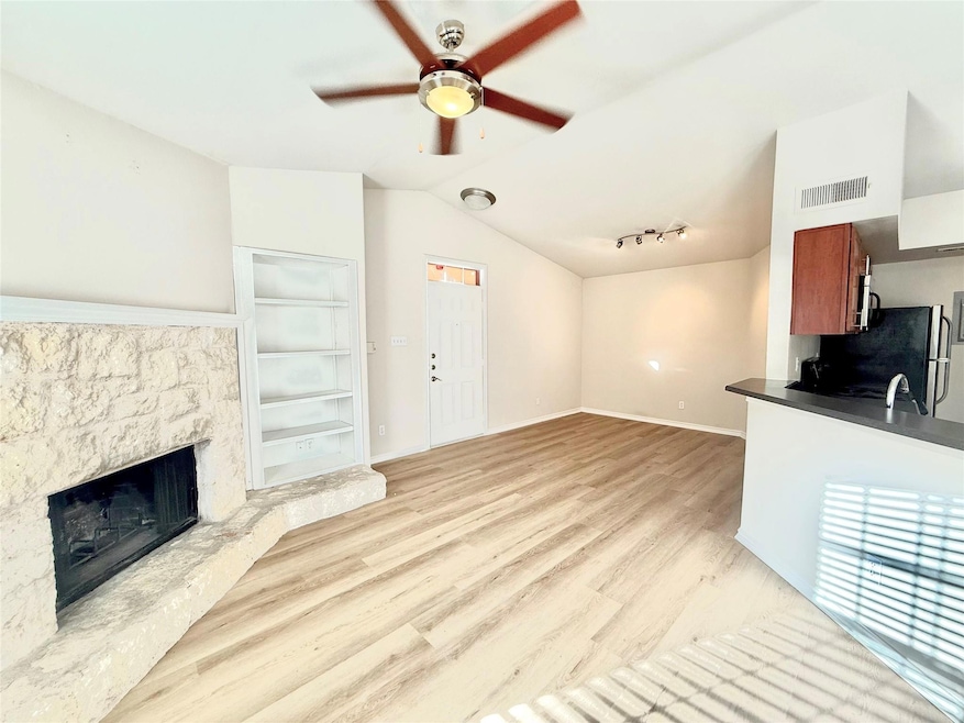 Unfurnished living room with a ceiling fan, lofted ceiling, light wood-type flooring, and a stone fireplace