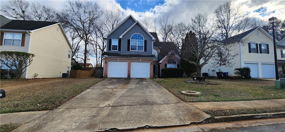 Traditional home featuring brick siding, an attached garage, driveway, a front lawn, and central air condition unit