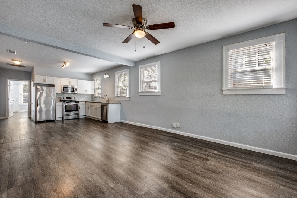 Unfurnished living room featuring plenty of natural light, dark wood-type flooring, a textured ceiling, a ceiling fan, and beam ceiling
