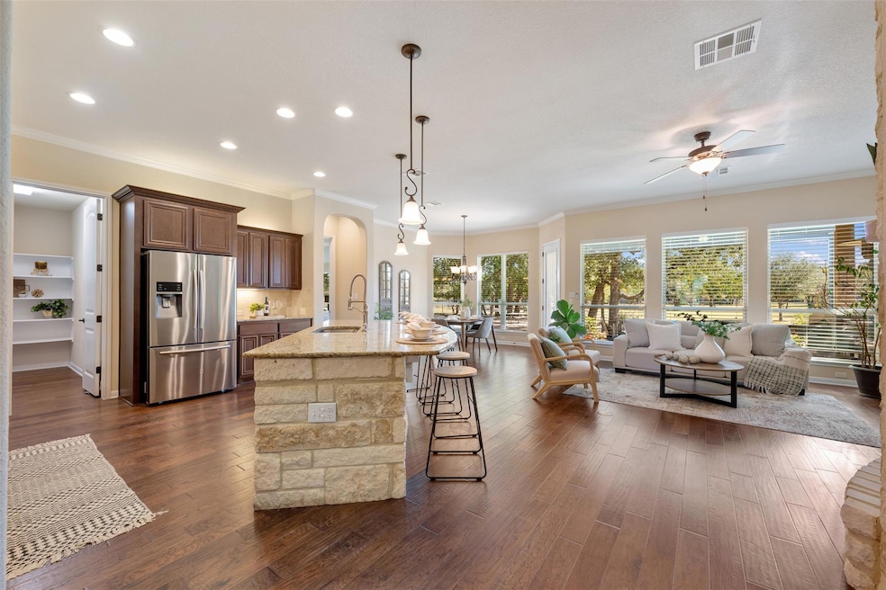 Kitchen with ornamental molding, stainless steel fridge with ice dispenser, a breakfast bar area, hanging light fixtures, and open floor plan