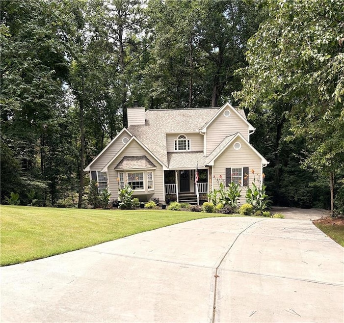 View of front facade featuring concrete driveway, covered porch, a chimney, a front yard, and roof with shingles