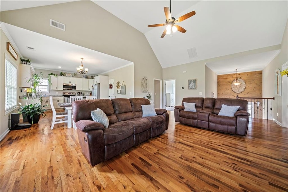 Living room featuring a chandelier, light wood-style flooring, a ceiling fan, high vaulted ceiling, and baseboards