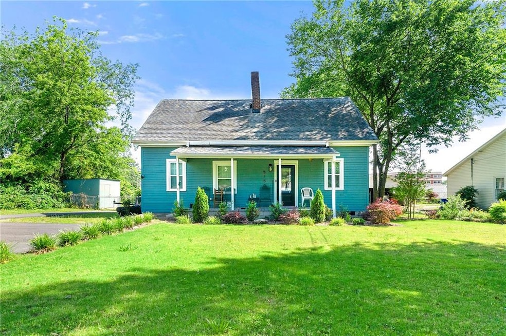 View of front facade featuring a porch, a front lawn, a chimney, and a shingled roof