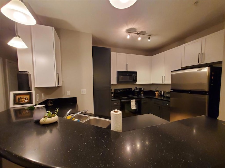 Kitchen with black appliances, a peninsula, white cabinetry, and dark stone counters
