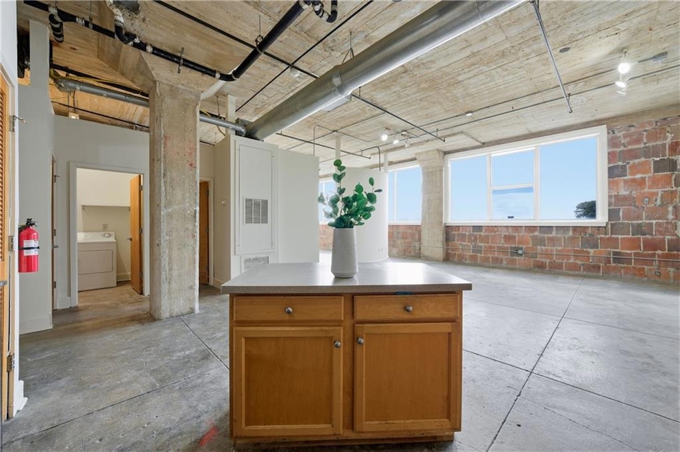 Kitchen with brown cabinetry, concrete floors, washer / dryer, and a center island