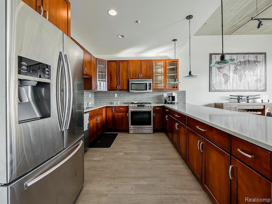 Kitchen featuring appliances with stainless steel finishes, glass insert cabinets, tasteful backsplash, light wood-type flooring, and pendant lighting