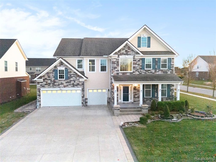 View of front of house with stone siding, a porch, a front lawn, a garage, and driveway
