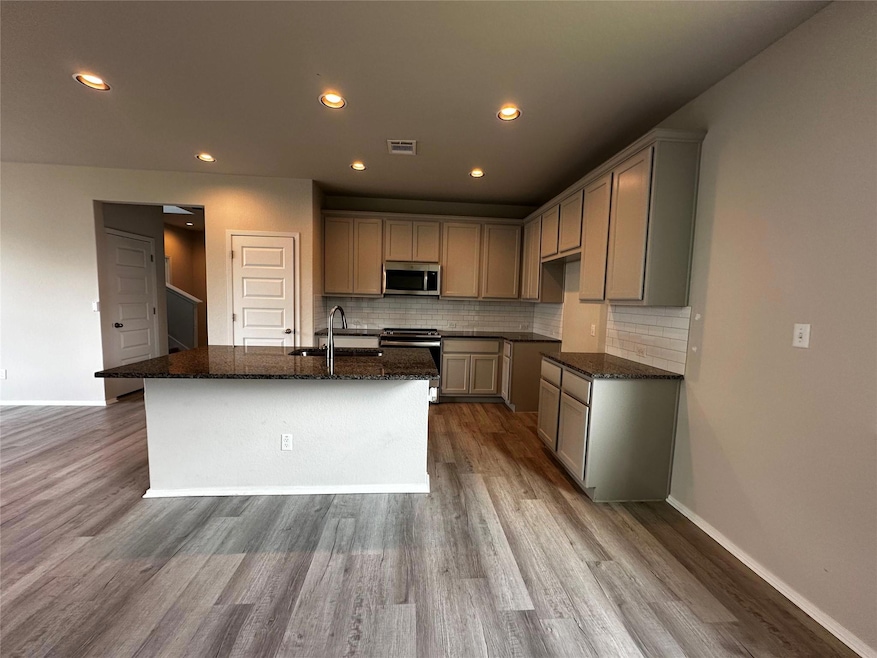 Kitchen featuring dark stone counters, range, backsplash, stainless steel microwave, and recessed lighting