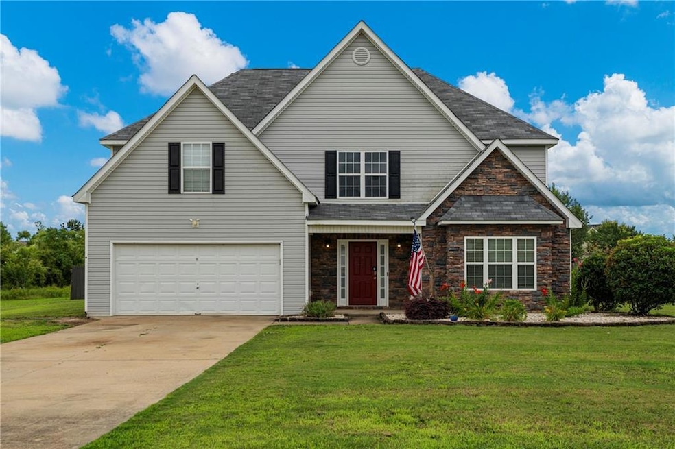 Traditional-style home featuring an attached garage, stone siding, a front yard, and driveway
