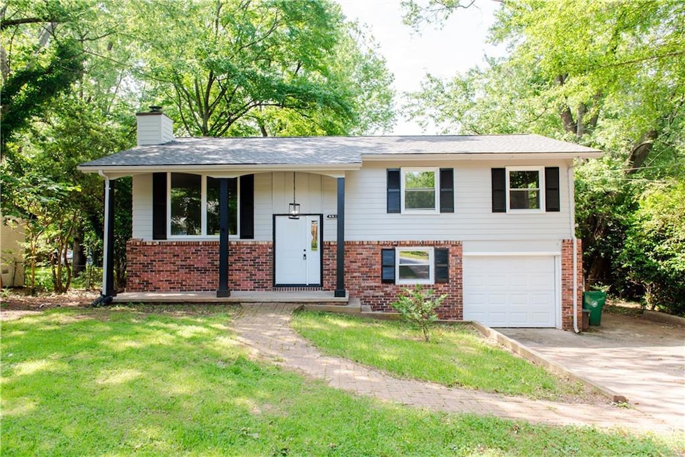 Raised ranch with a garage, a chimney, driveway, and brick siding