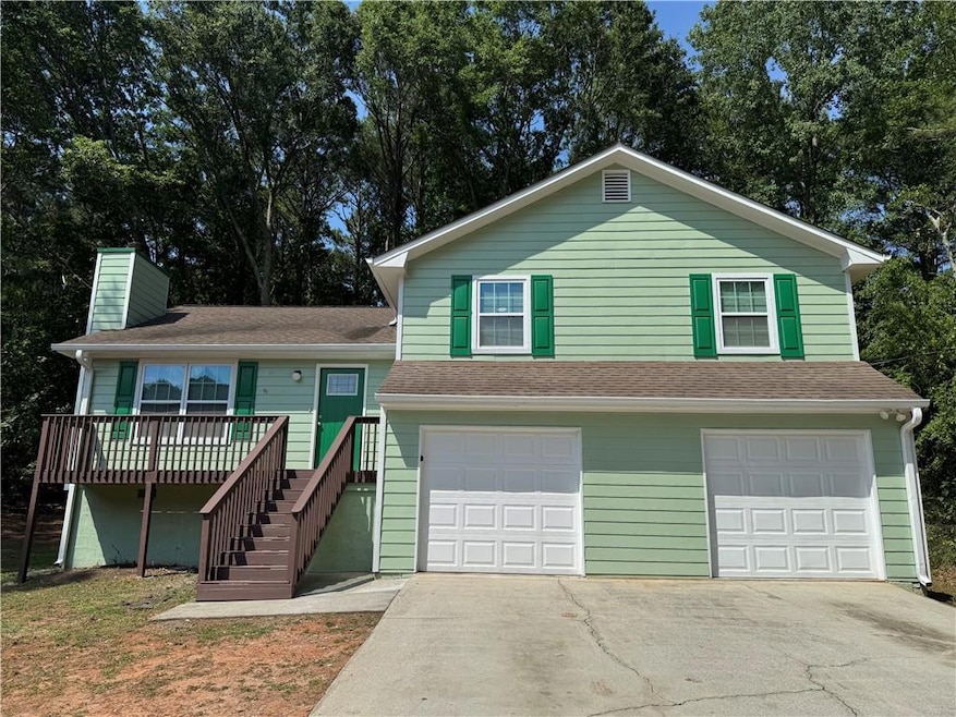 Tri-level home featuring an attached garage, stairway, asphalt driveway, a chimney, and a wooden deck