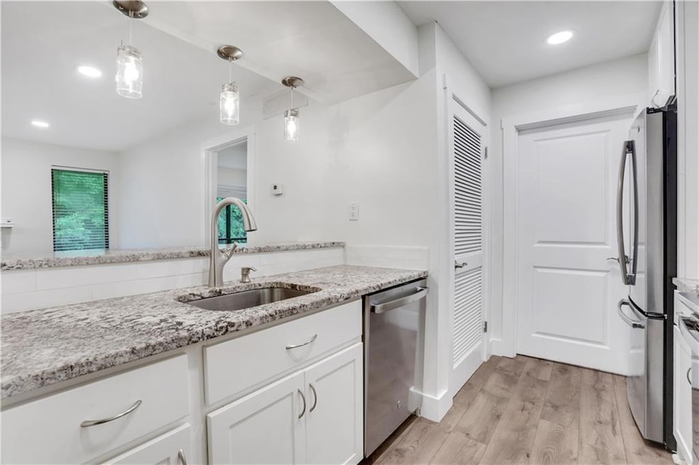 Kitchen with appliances with stainless steel finishes, a sink, white cabinetry, light wood-type flooring, and light stone counters