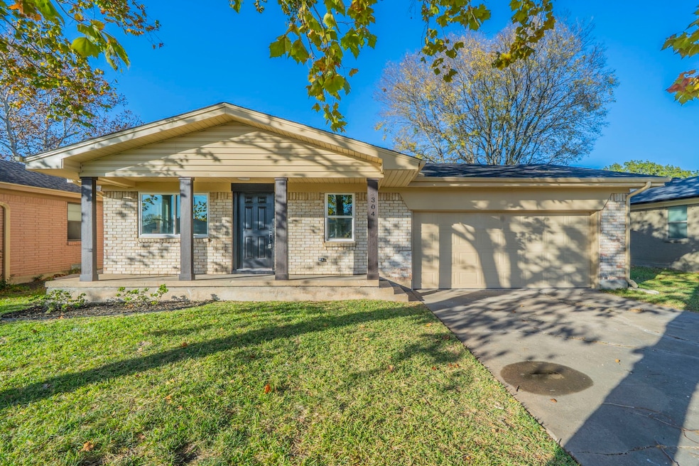 View of front of home with a porch, driveway, a front lawn, brick siding, and an attached garage