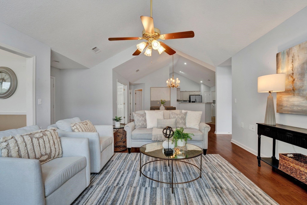 Living room featuring ceiling fan with notable chandelier, lofted ceiling, and wood-type flooring