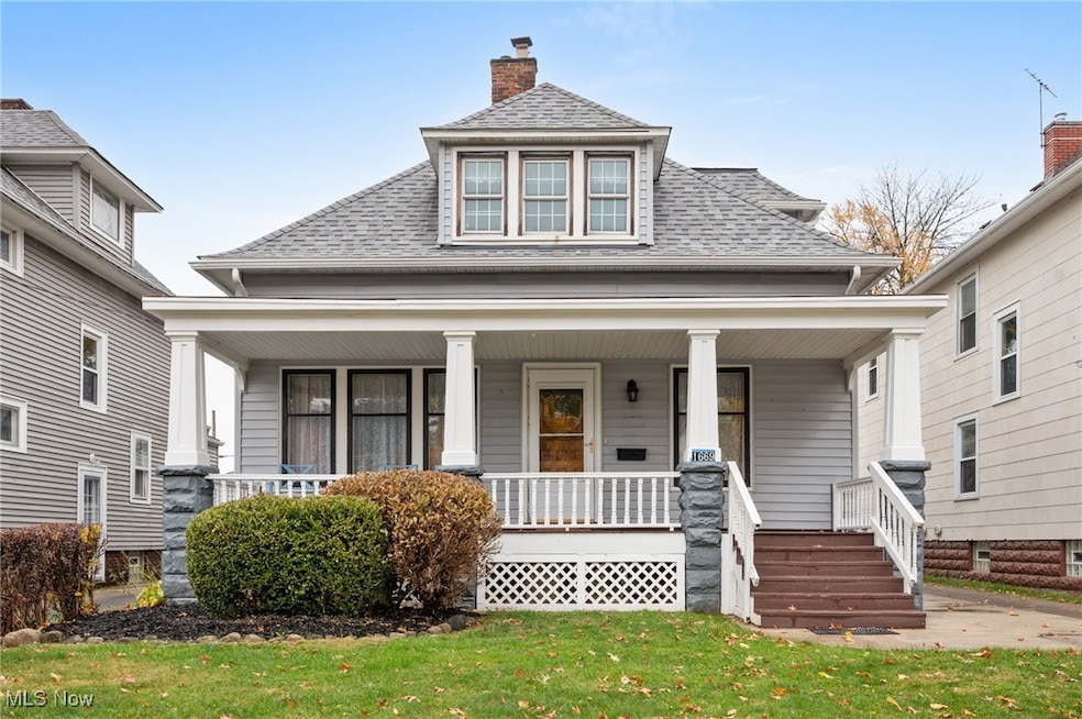View of front facade with a shingled roof, a porch, a chimney, and a front lawn