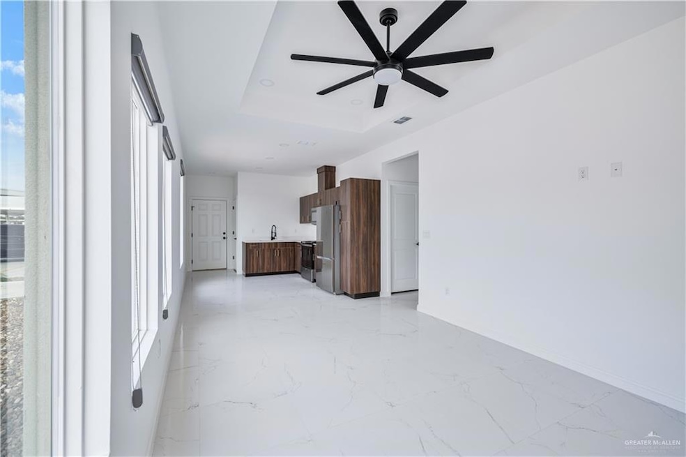 Unfurnished living room featuring ceiling fan, a raised ceiling, light marble finish flooring, and healthy amount of natural light
