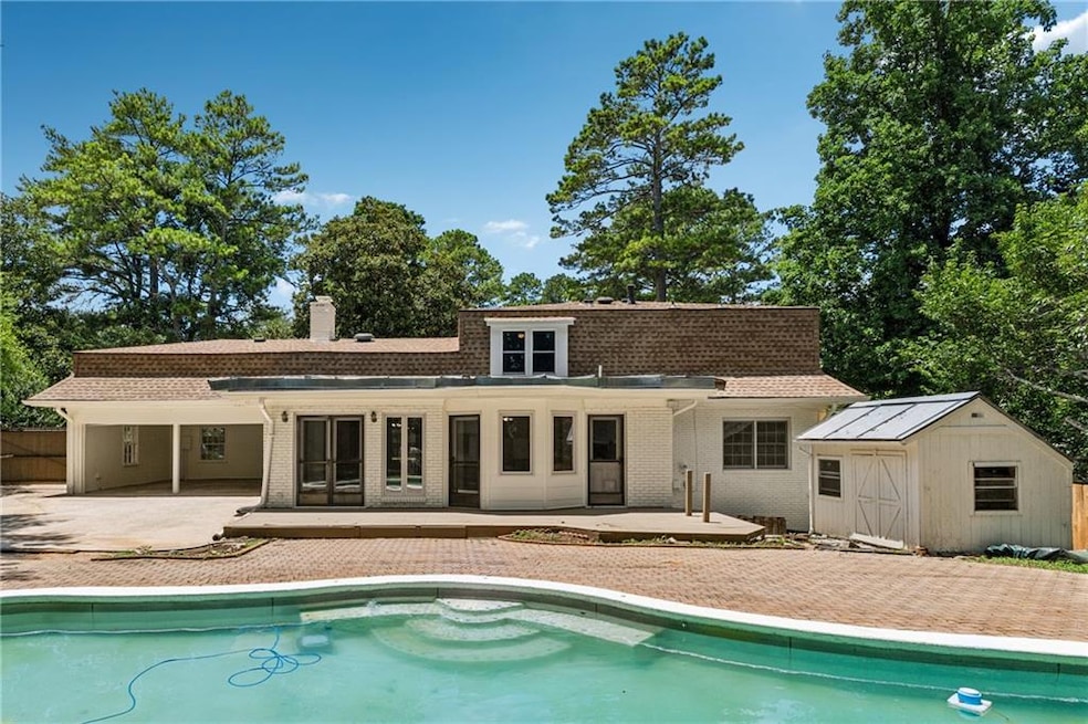 Rear view of house with a patio, an outdoor pool, a storage shed, brick siding, and a chimney