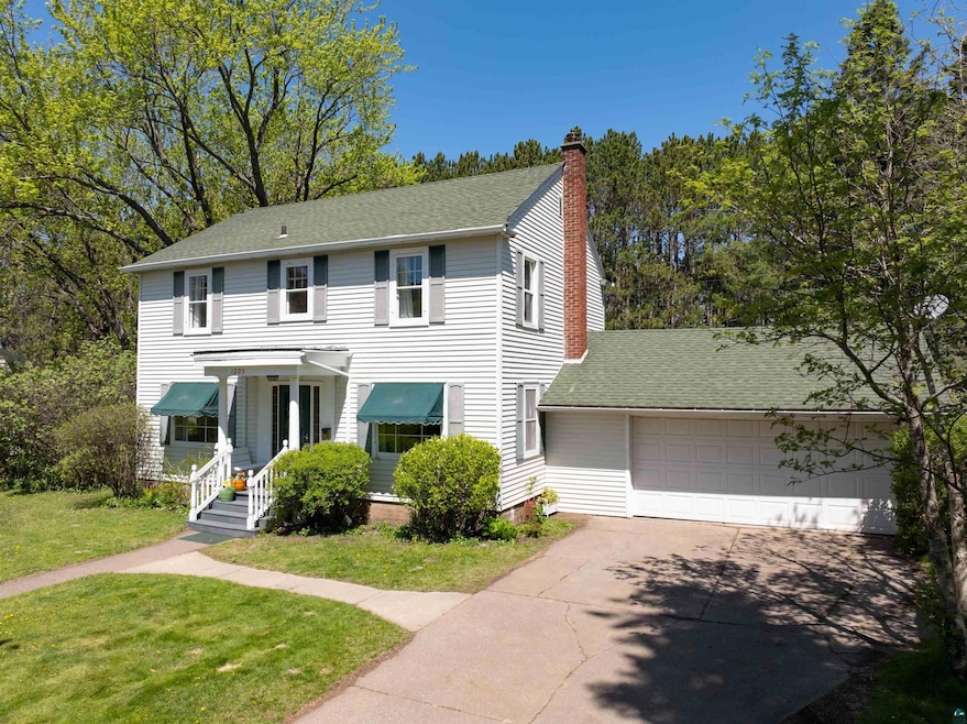 View of front of property featuring a garage, a chimney, driveway, a front yard, and a shingled roof