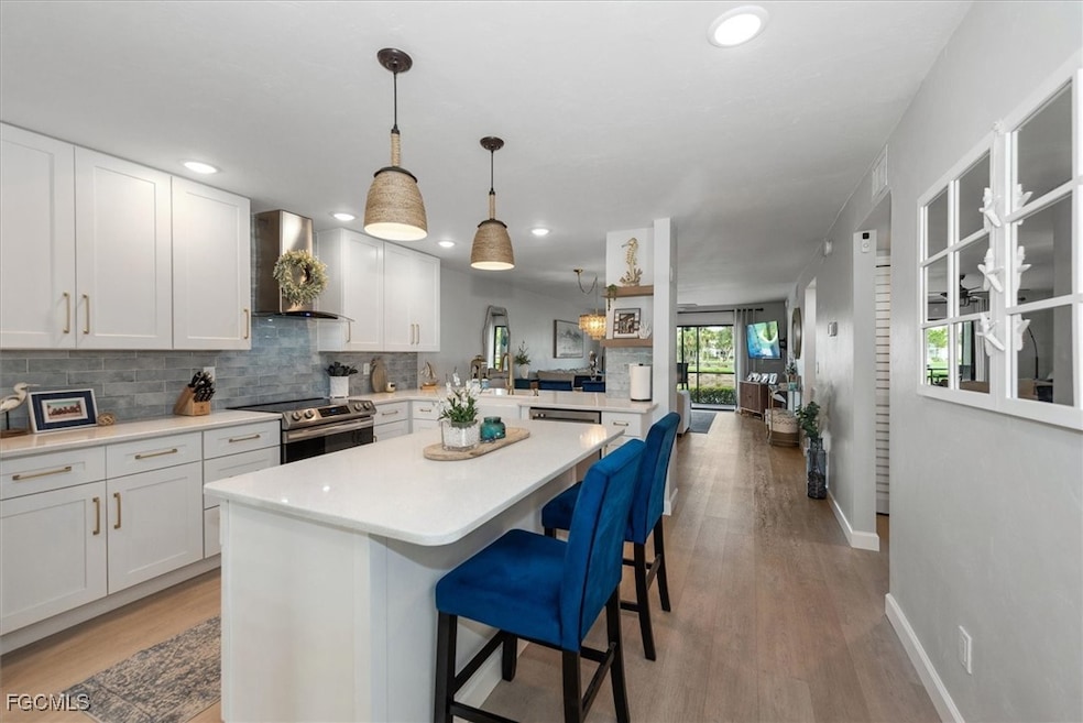 Kitchen with white cabinetry, a kitchen breakfast bar, decorative backsplash, electric range, and wall chimney exhaust hood