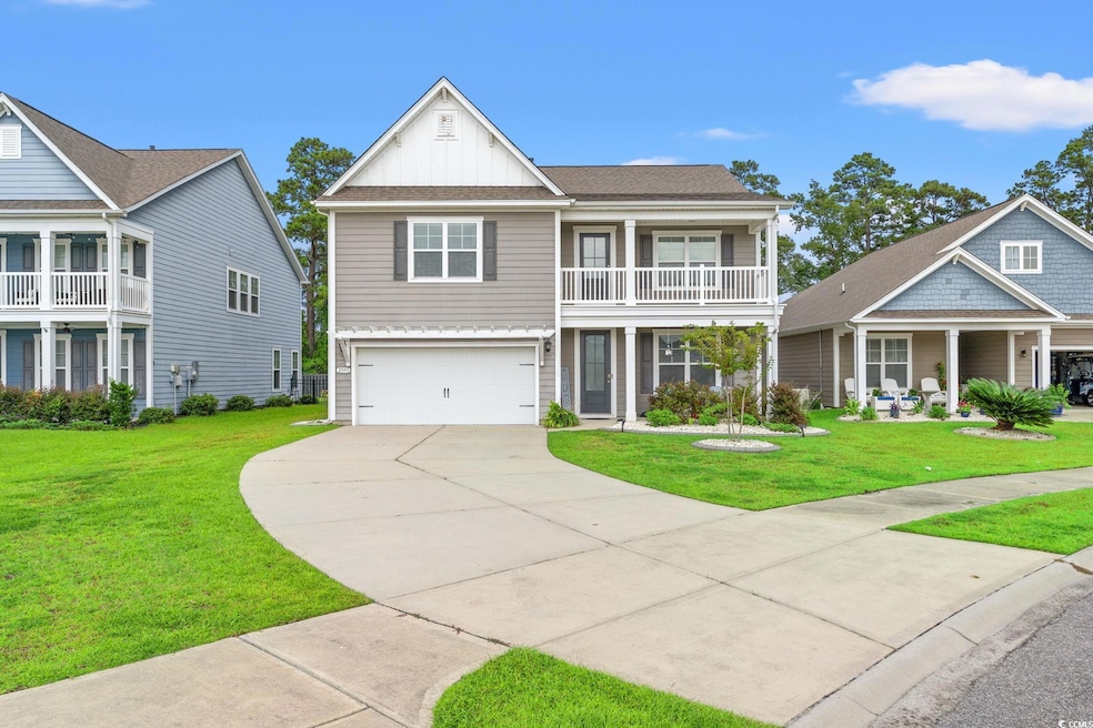 View of front of home with board and batten siding, concrete driveway, an attached garage, a front lawn, and a balcony