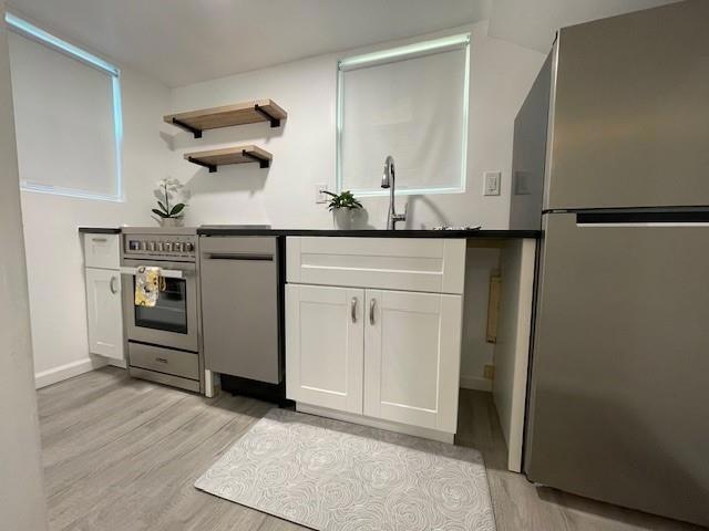 Kitchen with appliances with stainless steel finishes, light wood finished floors, white cabinets, a sink, and dark countertops