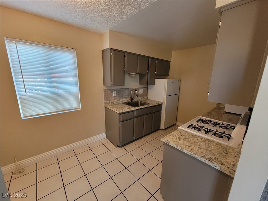 Kitchen featuring decorative backsplash, light tile patterned flooring, a textured ceiling, white appliances, and light stone countertops