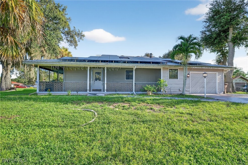 View of front of property featuring roof mounted solar panels, a garage, a front lawn, driveway, and a porch