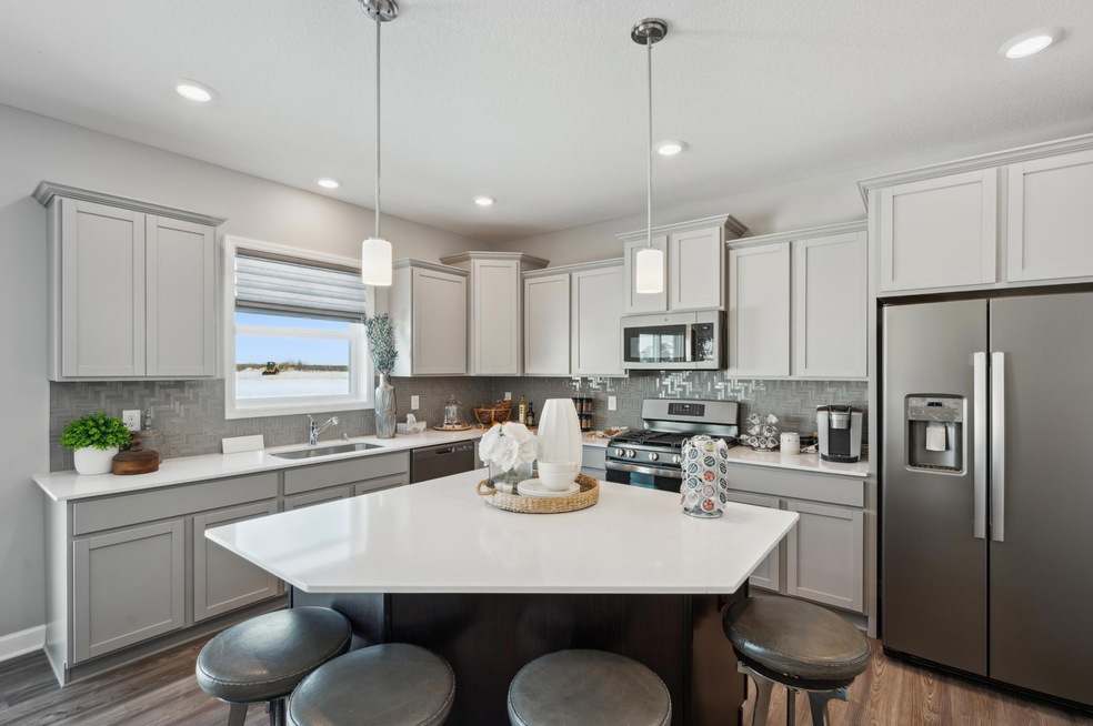 This spacious kitchen features a large center island, quartz countertops, recessed lighting, LVP wood floors, stainless appliances and more! (Photo of decorated model, actual home's finishes may vary slightly)