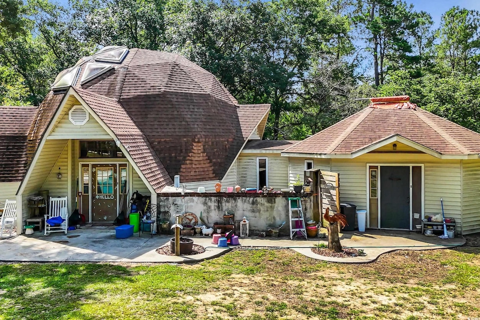 View of front of house featuring a patio area, roof with shingles, a front lawn, and view of scattered trees