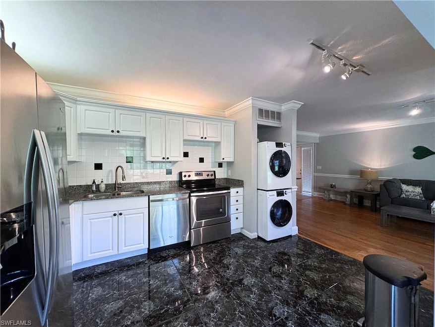 Kitchen with appliances with stainless steel finishes, stacked washer / dryer, a sink, ornamental molding, and open floor plan
