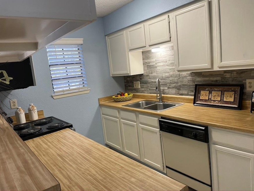 Kitchen with a textured wall, dishwasher, tasteful backsplash, white cabinets, and electric range