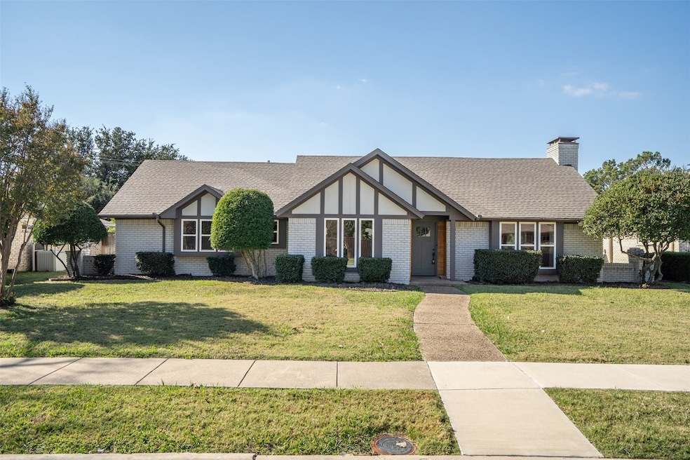 Tudor home with a front yard, a shingled roof, a chimney, and brick siding