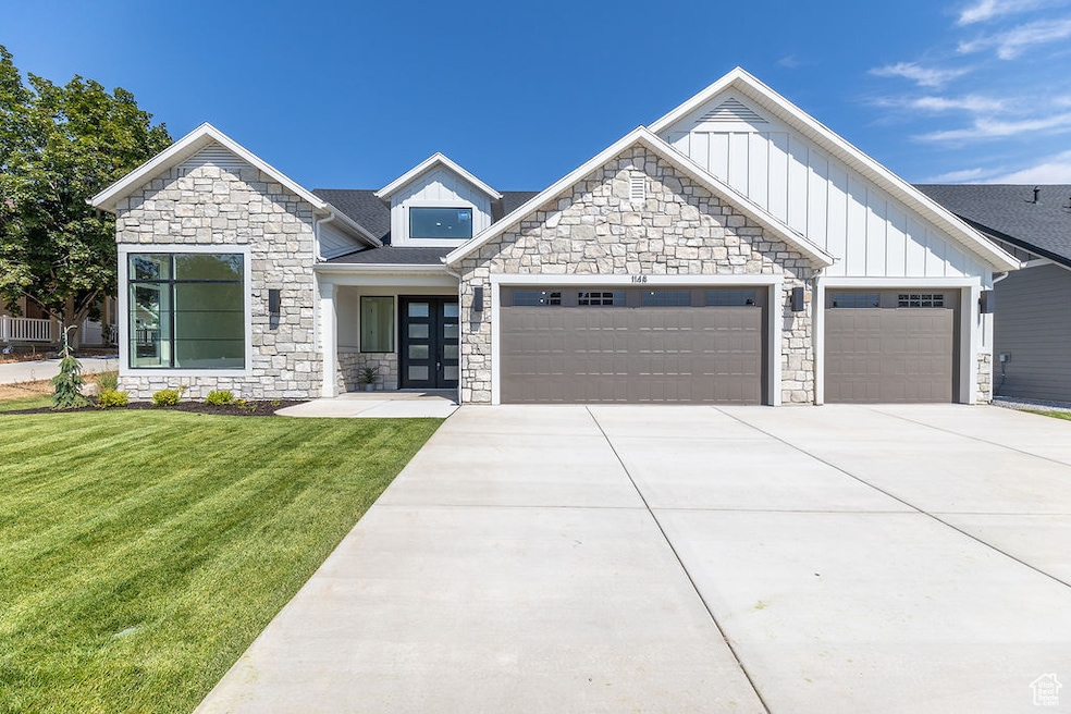 View of front of home with stone siding, a garage, a front yard, and board and batten siding