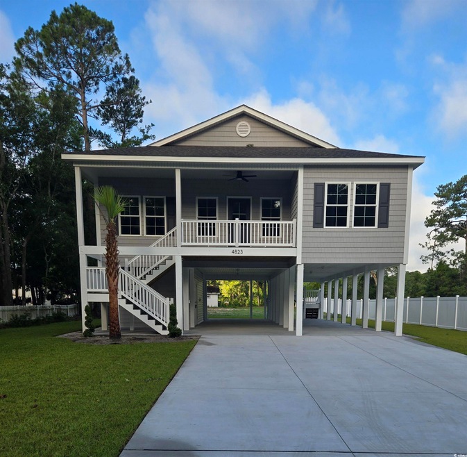 Coastal inspired home featuring a carport, a ceiling fan, driveway, a porch, and stairs