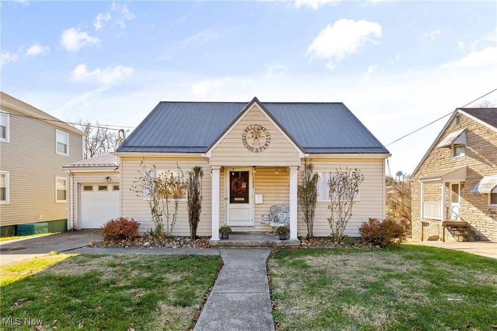 View of front of house with a front yard, a metal roof, covered porch, a garage, and driveway