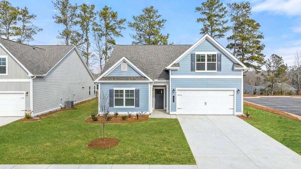 Traditional-style home featuring driveway, central air condition unit, an attached garage, a front lawn, and roof with shingles
