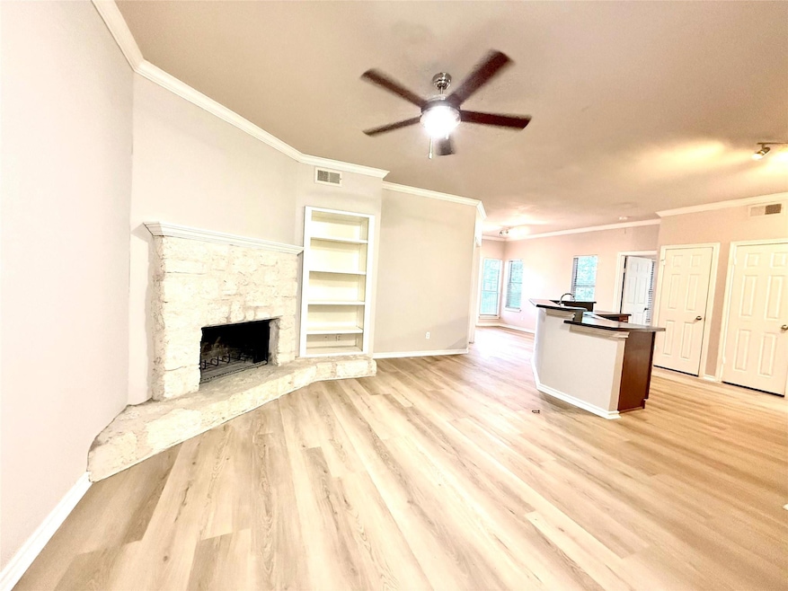 Unfurnished living room featuring crown molding, ceiling fan, light wood-type flooring, and a fireplace