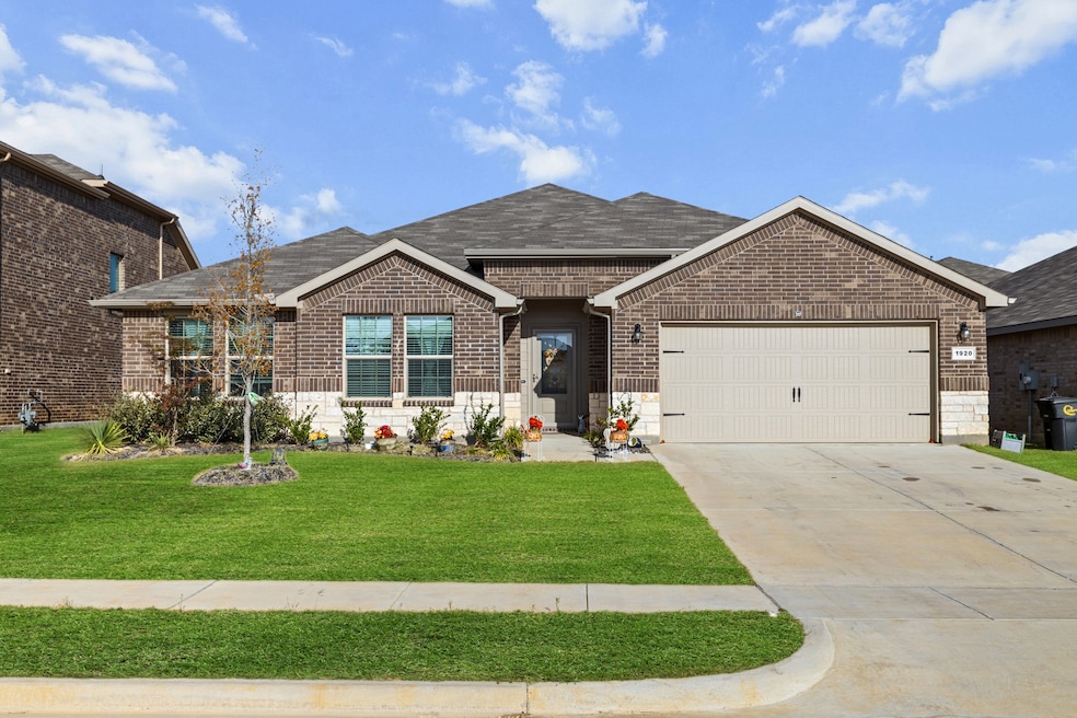 Single story home featuring an attached garage, driveway, brick siding, a front yard, and roof with shingles